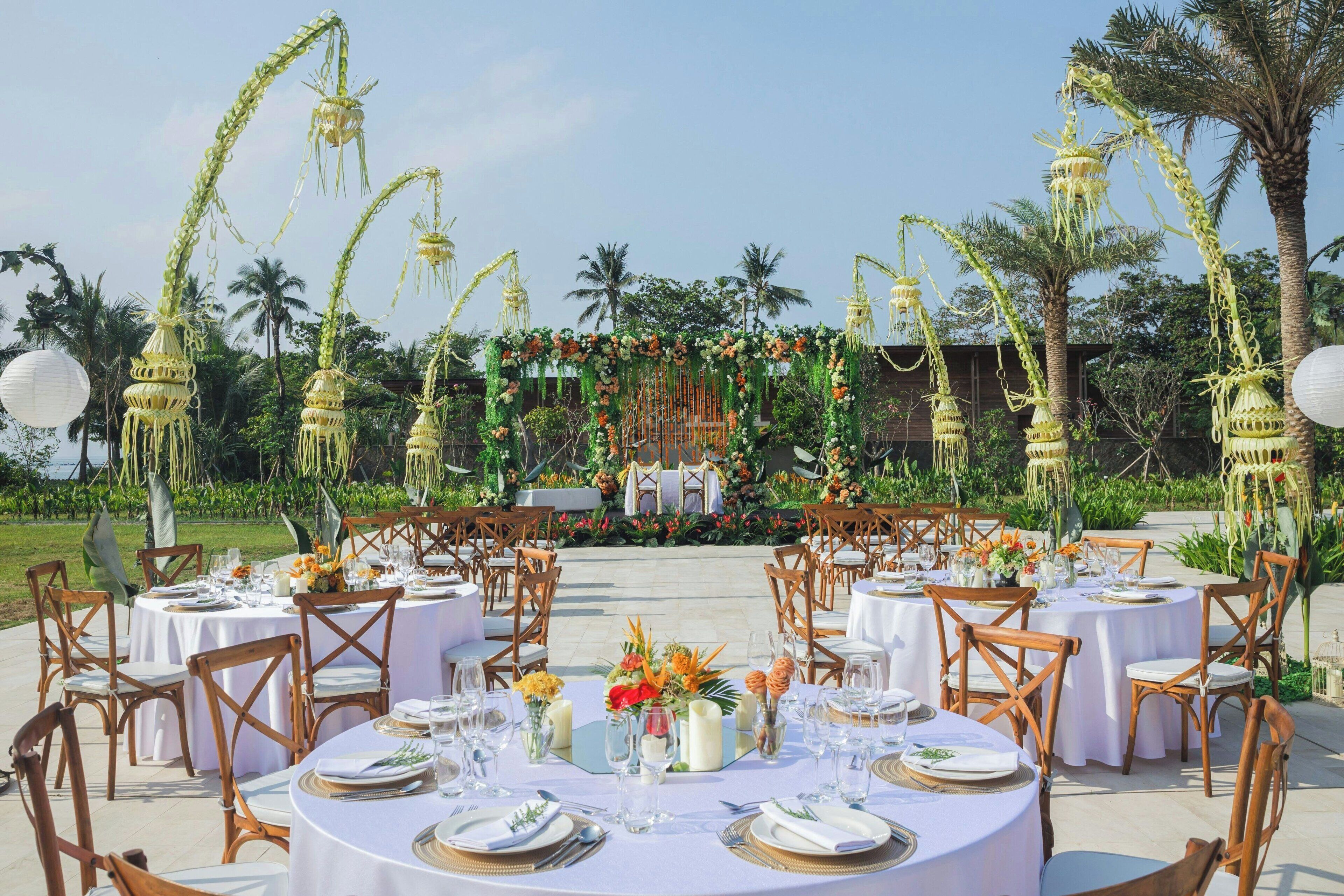 An outdoor dining area with round tables set for a meal, surrounded by wooden chairs.