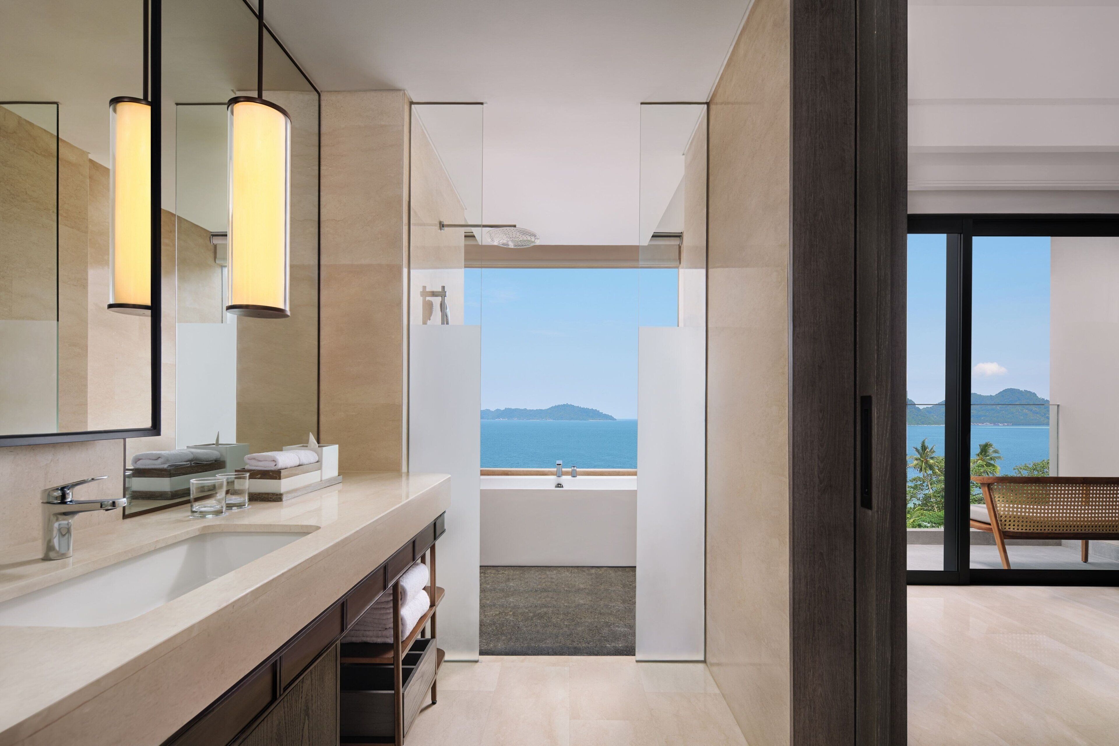 A modern bathroom with a large mirror, a sink, and a bathtub. There is a view of the ocean through a glass door.