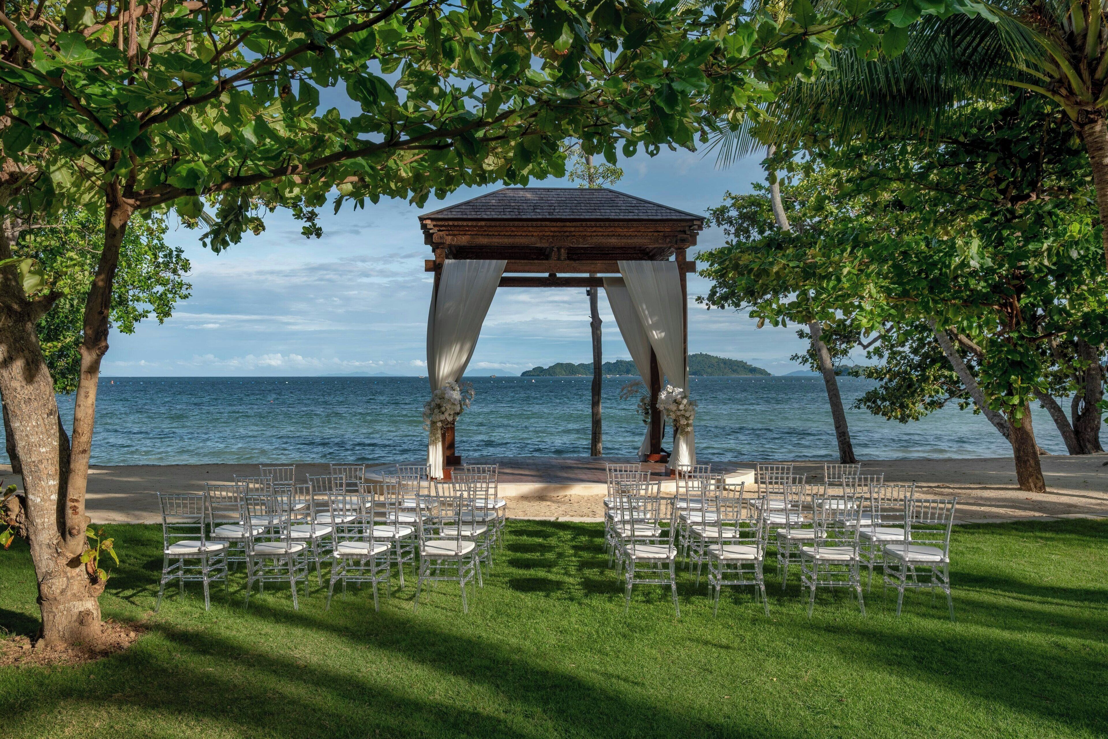 A gazebo with a view of the sea, surrounded by chairs and trees.
