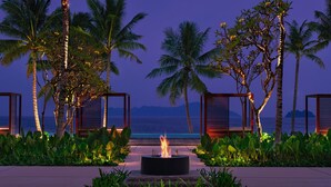 A fire pit surrounded by lush greenery and palm trees, with a view of the ocean at dusk. - Lampung Marriott Resort & Spa (Bandar Lampung)