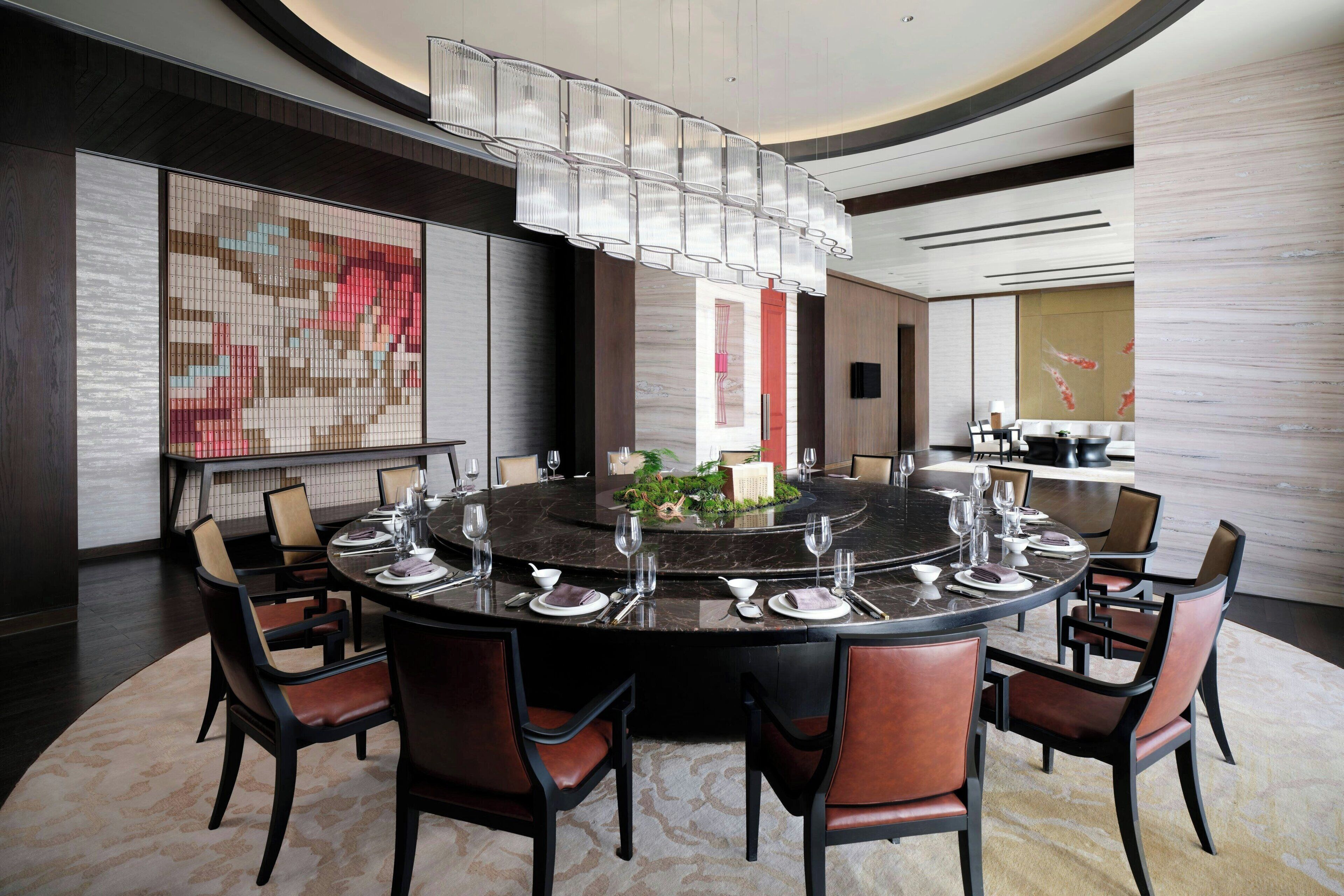A modern dining area with a round table set for six, surrounded by leather chairs.