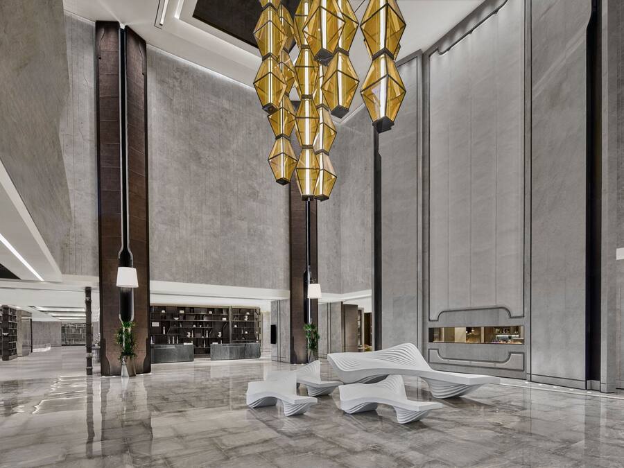 A spacious lobby with a modern chandelier, a reception desk, and a seating area.
