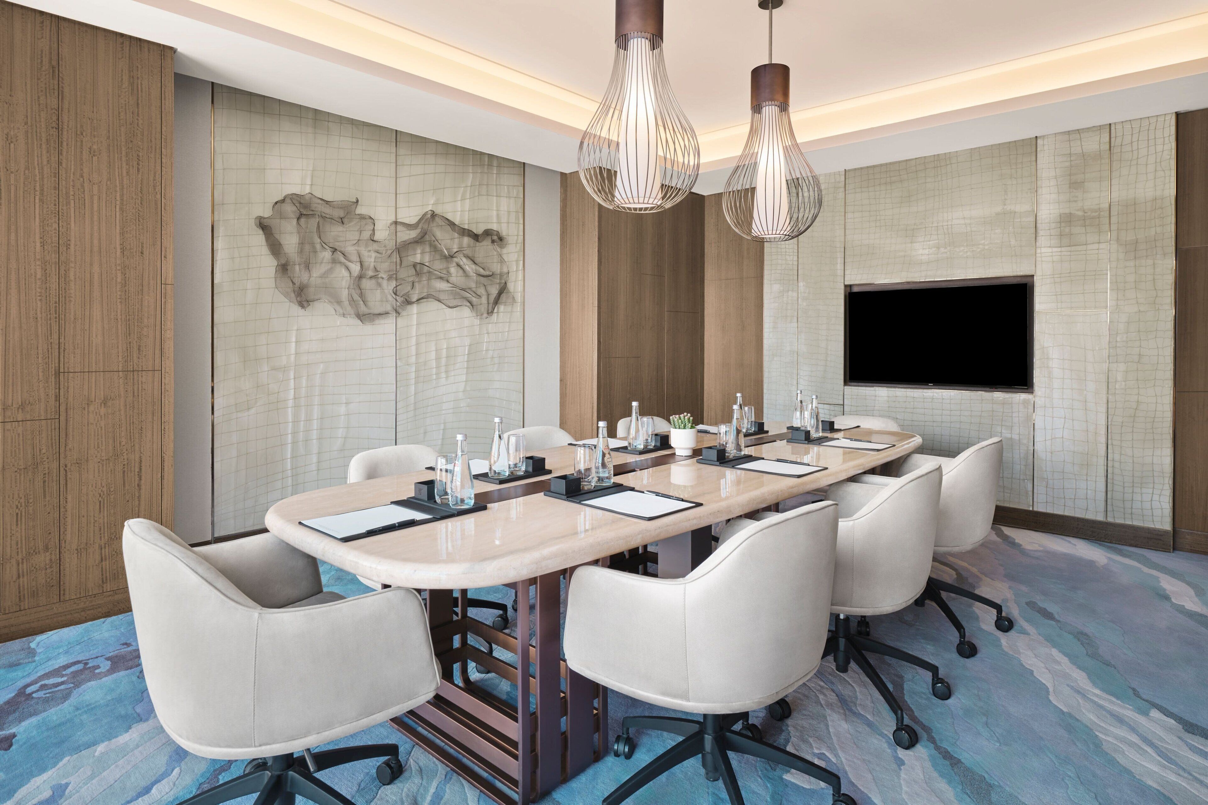 A conference room with a long table, white chairs, and a flat-screen TV on the wall.