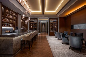 Zona de bar moderna con encimera de mármol, estanterías de madera y área de estar con sillones tapizados.