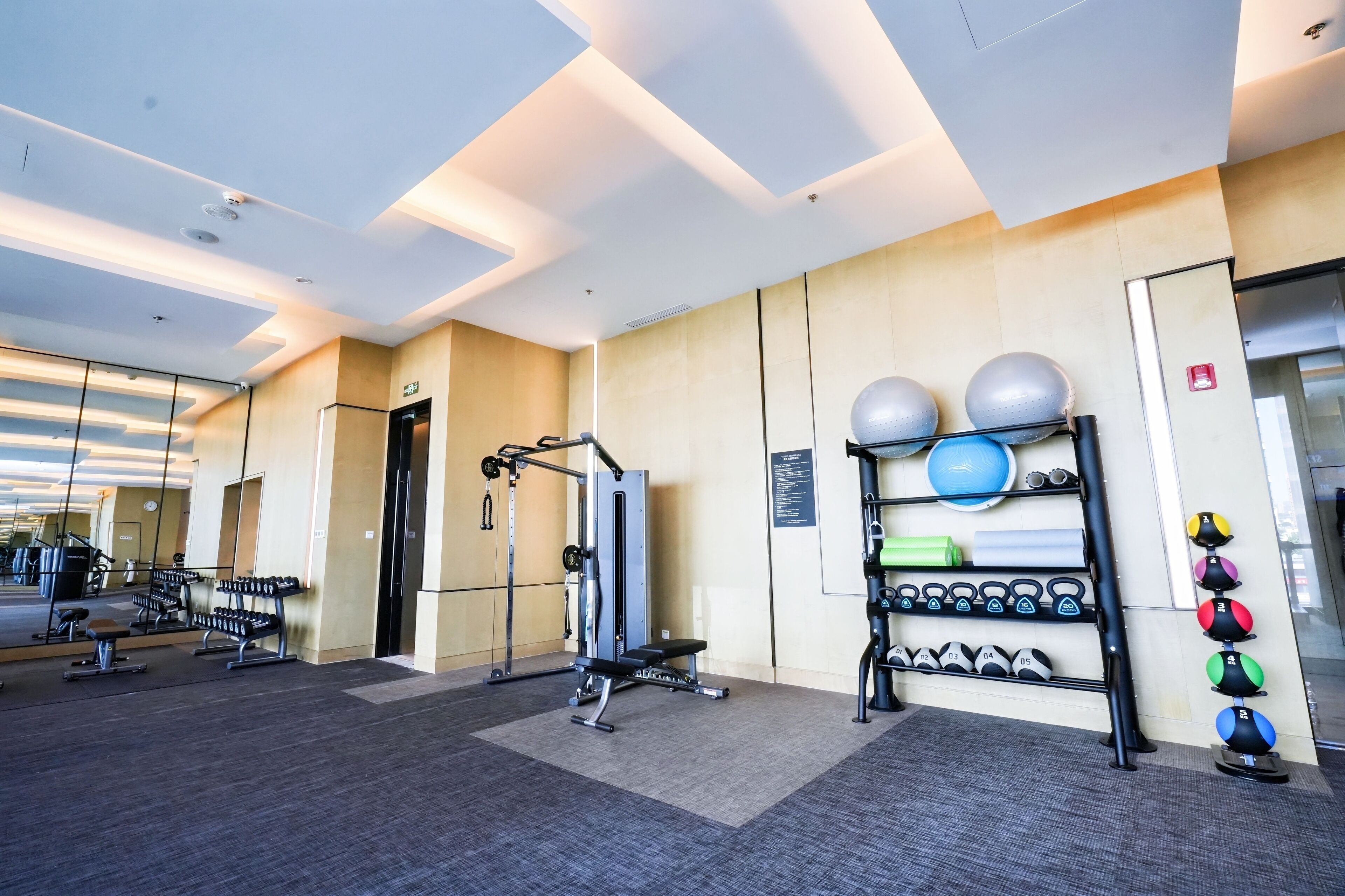 A modern gym with exercise equipment, a mirrored wall, and a variety of weights.