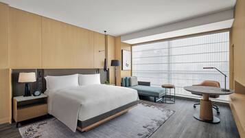 Et moderne hotelværelse med en stor seng, sengeborde, et skrivebord og udsigt gennem store vinduer.