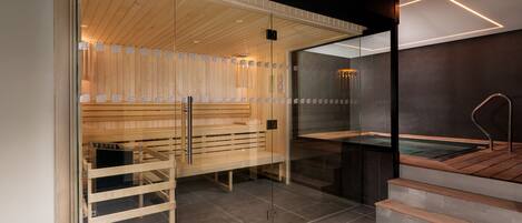 A modern sauna with wooden benches and glass walls, a heated floor, and a separate area with a hot tub.