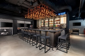 Zona de bar moderna con mostrador, varios taburetes y una amplia selección de licores.