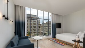Une chambre d’hôtel moderne dotée d’une grande fenêtre, d’un canapé, d’un lit, d’une petite table et d’un téléviseur.