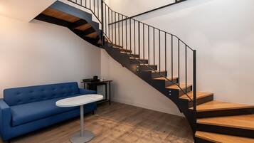 A modern interior with a blue sofa, a small round table, and a spiral staircase with wooden steps and black railings.