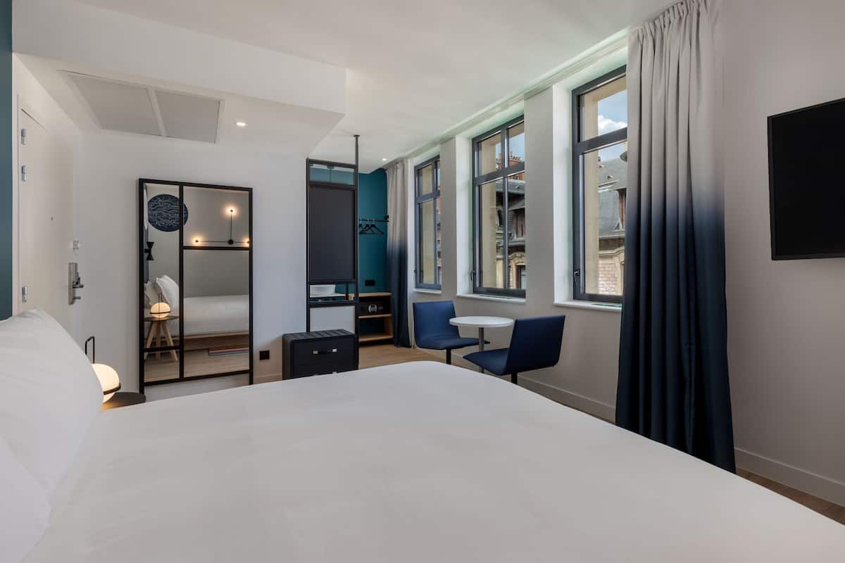 Ein modernes Hotelzimmer mit einem großen Bett, einem Schreibtisch, einem Stuhl, einem kleinen Tisch und einem Kleiderschrank.