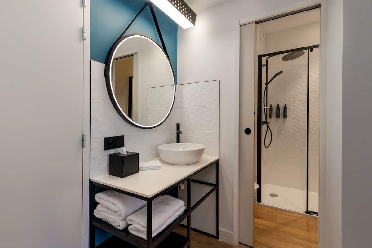 Un baño moderno con un lavamanos blanco, un mueble negro y un espejo redondo.