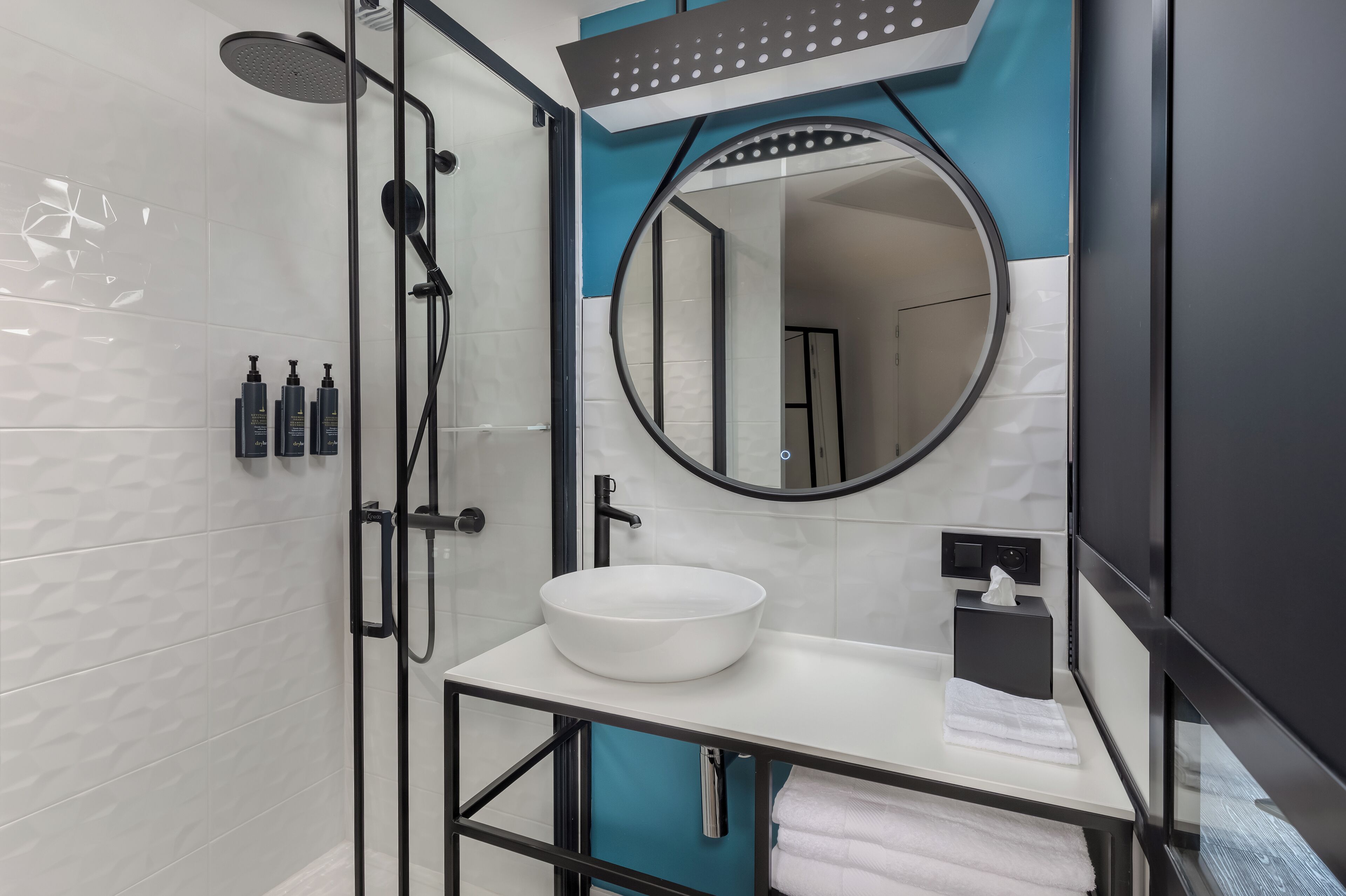 Un bagno moderno con un lavandino bianco, uno specchio rotondo e una cabina doccia in vetro.