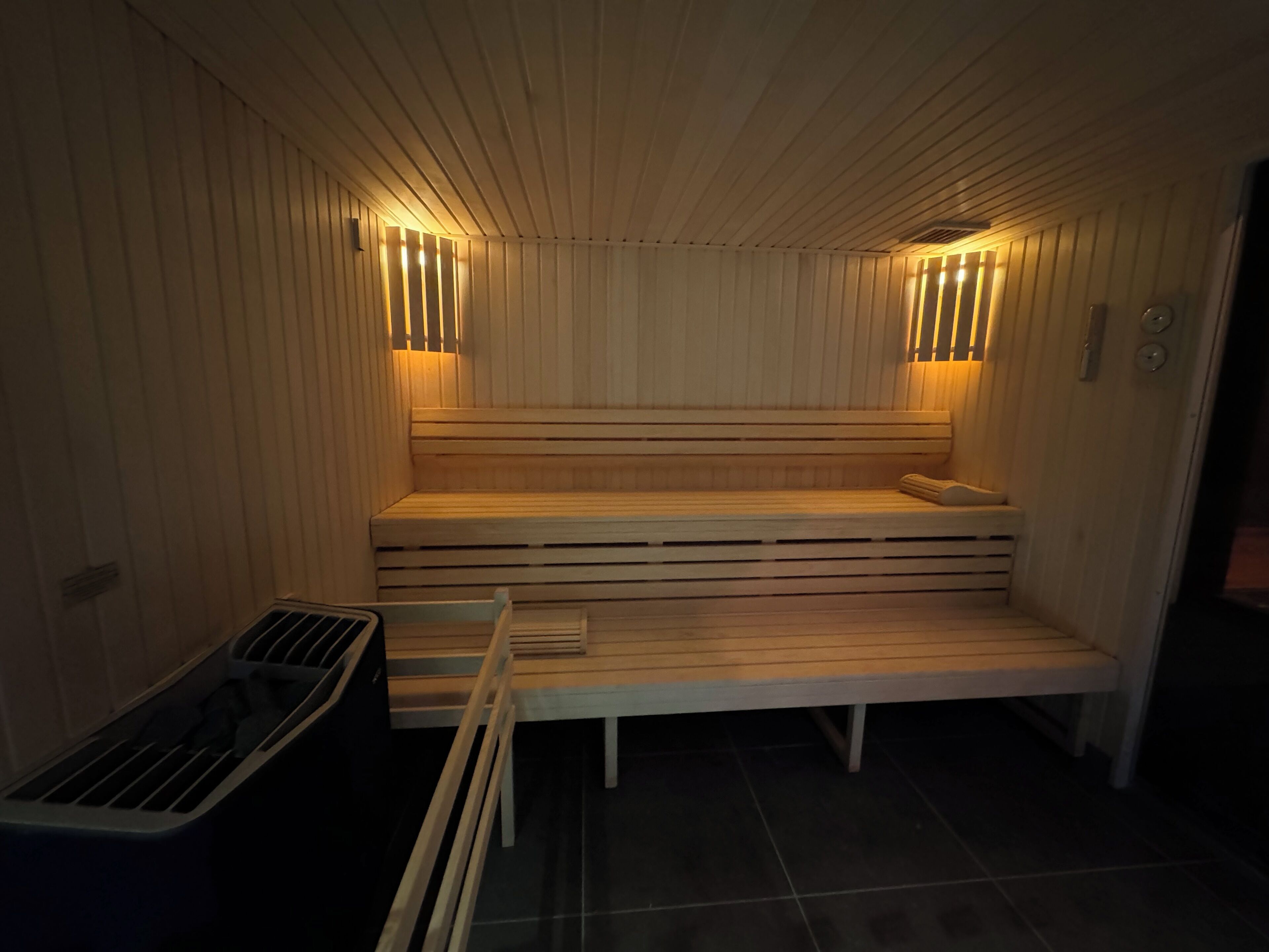 A sauna with wooden benches and slatted walls, equipped with wall-mounted lights.