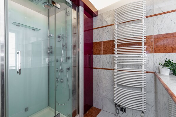 Un baño moderno con ducha envuelta en vidrio, un toallero blanco y pared revestida de mármol.