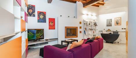 A modern living room with a purple sofa, a flat-screen TV, and artwork on the walls.