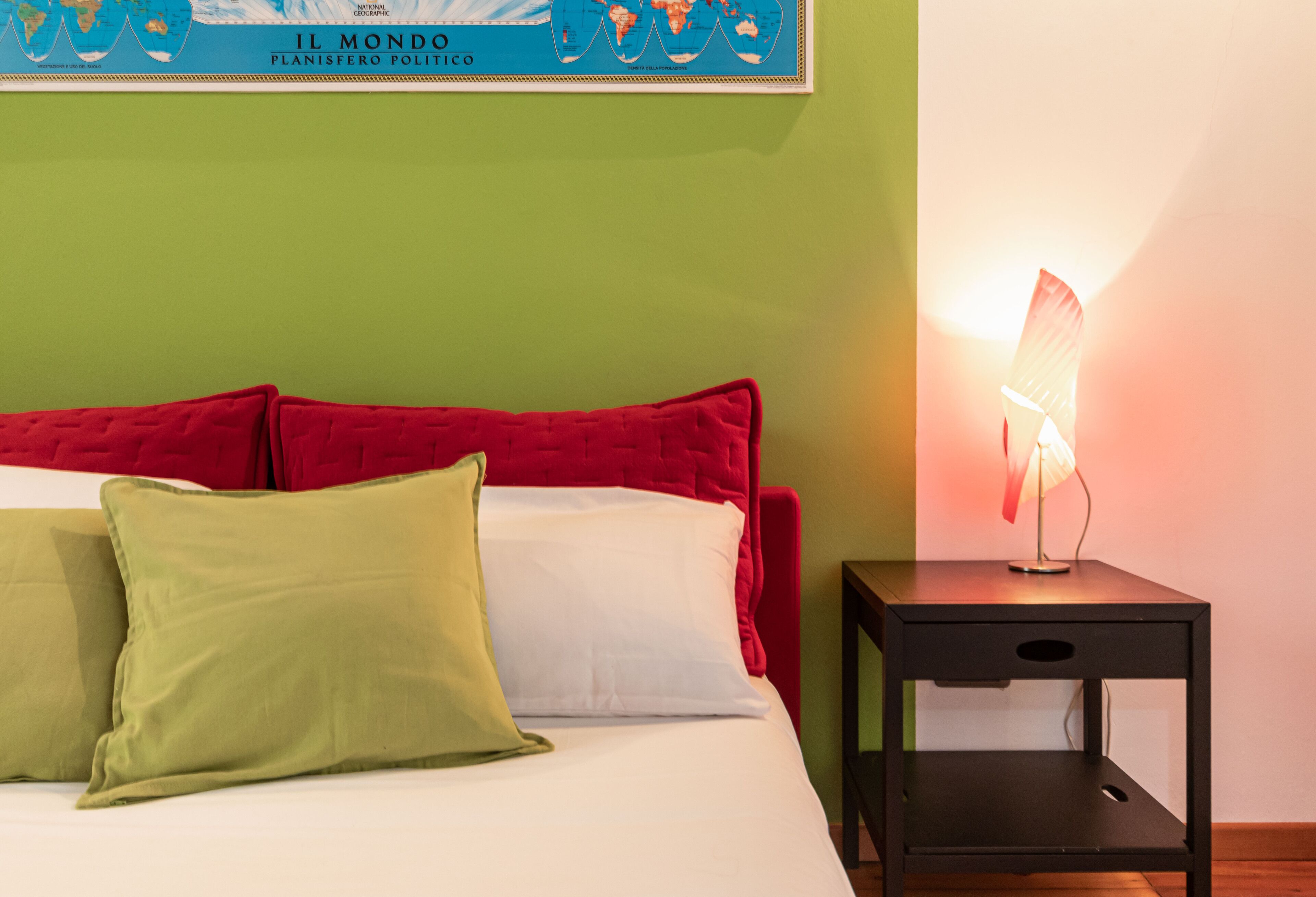 A bed with red and white bedding, a green pillow, and a nightstand with a lamp.