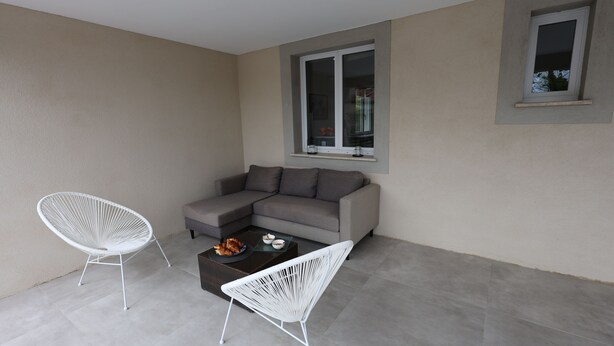 Et moderne opholdsområde med en grå sofa, to hvide stole og et sofabord med croissanter.