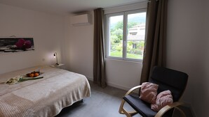 Et soveværelse med en seng, en stol, et vindue med gardiner, et sengebord med en lampe, og en vægmonteret aircondition.