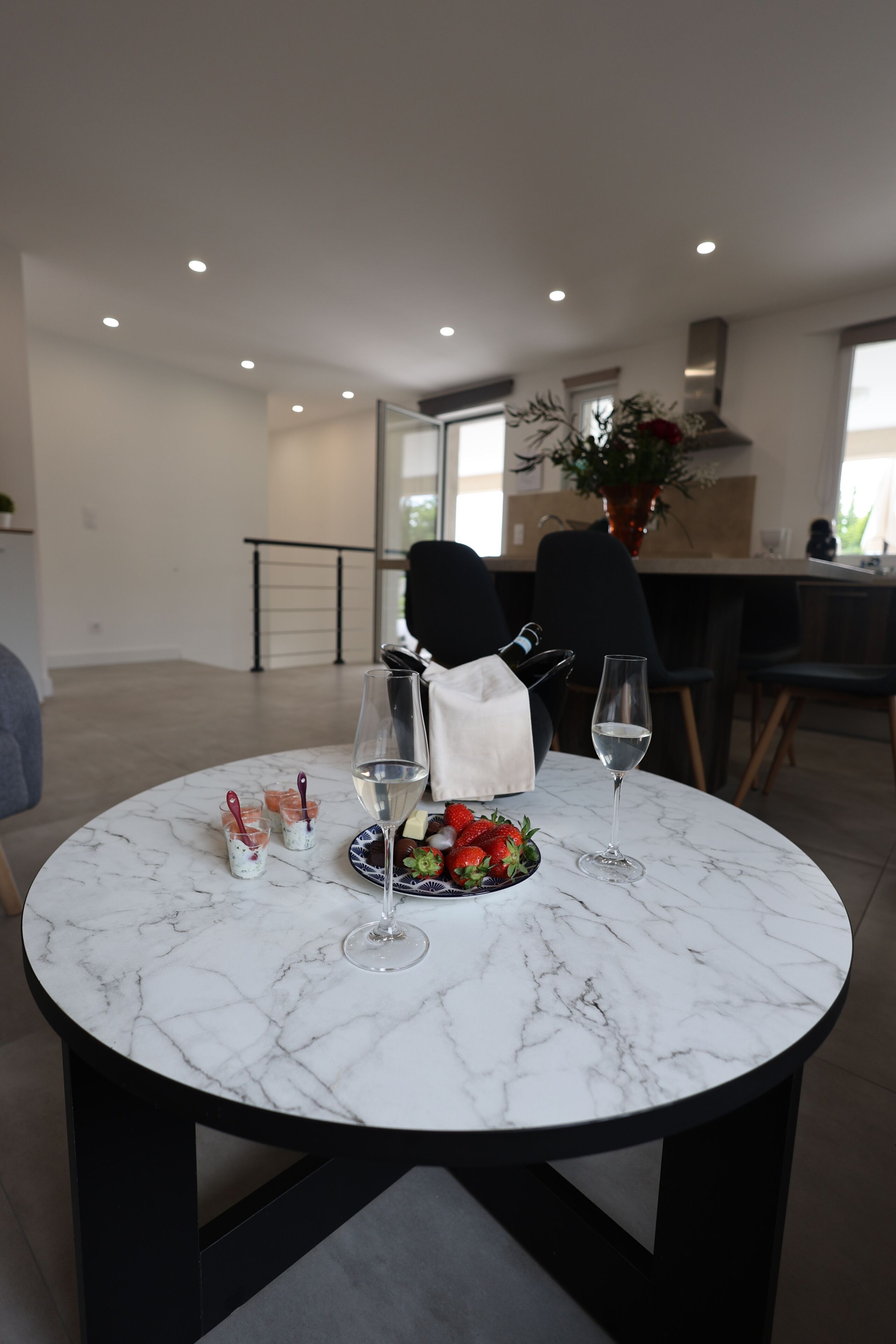 A modern dining area with a marble table, two wine glasses, a plate of strawberries, and a bottle of champagne.