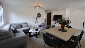 En moderne stue med en grå sofa, et rundt sofabord og et spiseområde med bord og stole.