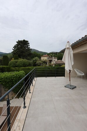 A terrace with a railing, a white umbrella, and a chair.