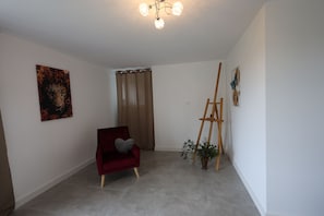 Una habitación con una silla roja, un cuadro, un caballete de madera y una planta en maceta.