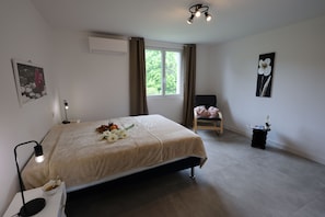 A bedroom with a bed, a chair, a window, and a bedside table.