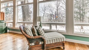 A wicker chair with patterned cushions in a room with large windows and a wooden floor. - Huge Retreat with Heated Pool And Hot Tub by Briggs Woods Walking Trail and Golf (Webster City)