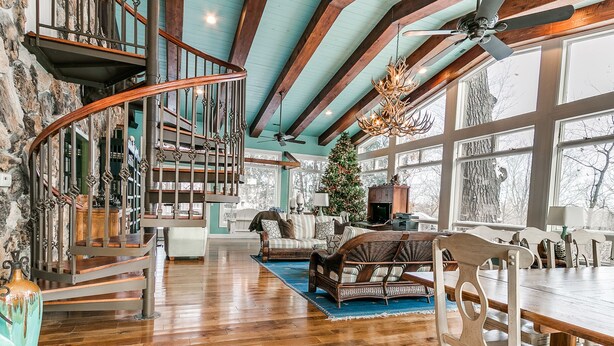 A spacious living area with a wooden staircase, a large window, and a Christmas tree. - Huge Retreat with Heated Pool And Hot Tub by Briggs Woods Walking Trail and Golf (Webster City)