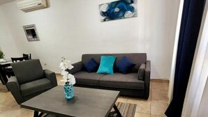 Un salon avec un canapé gris, deux fauteuils, une table basse ornée d’un vase et un tableau accroché au mur.