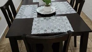 Un coin repas avec une table dressée pour quatre personnes, une plante en pot et un téléviseur en arrière-plan.