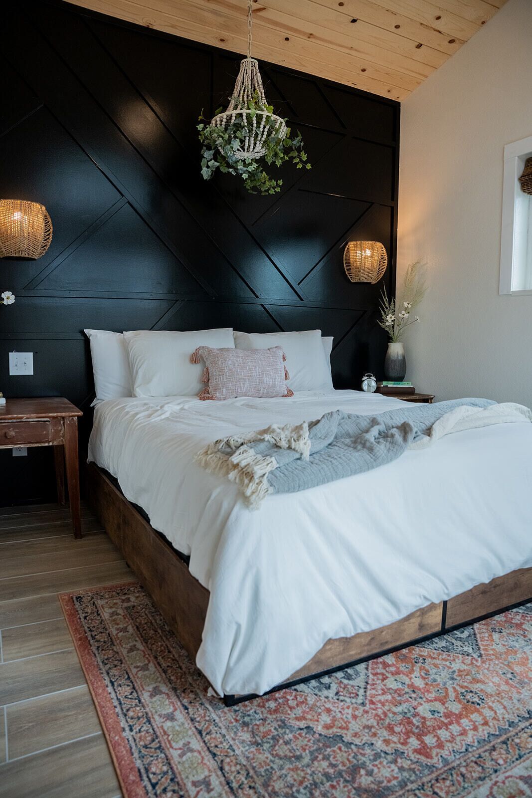 Een slaapkamer met een bed, een nachtkastje, een geweven lamp en een wandlamp.