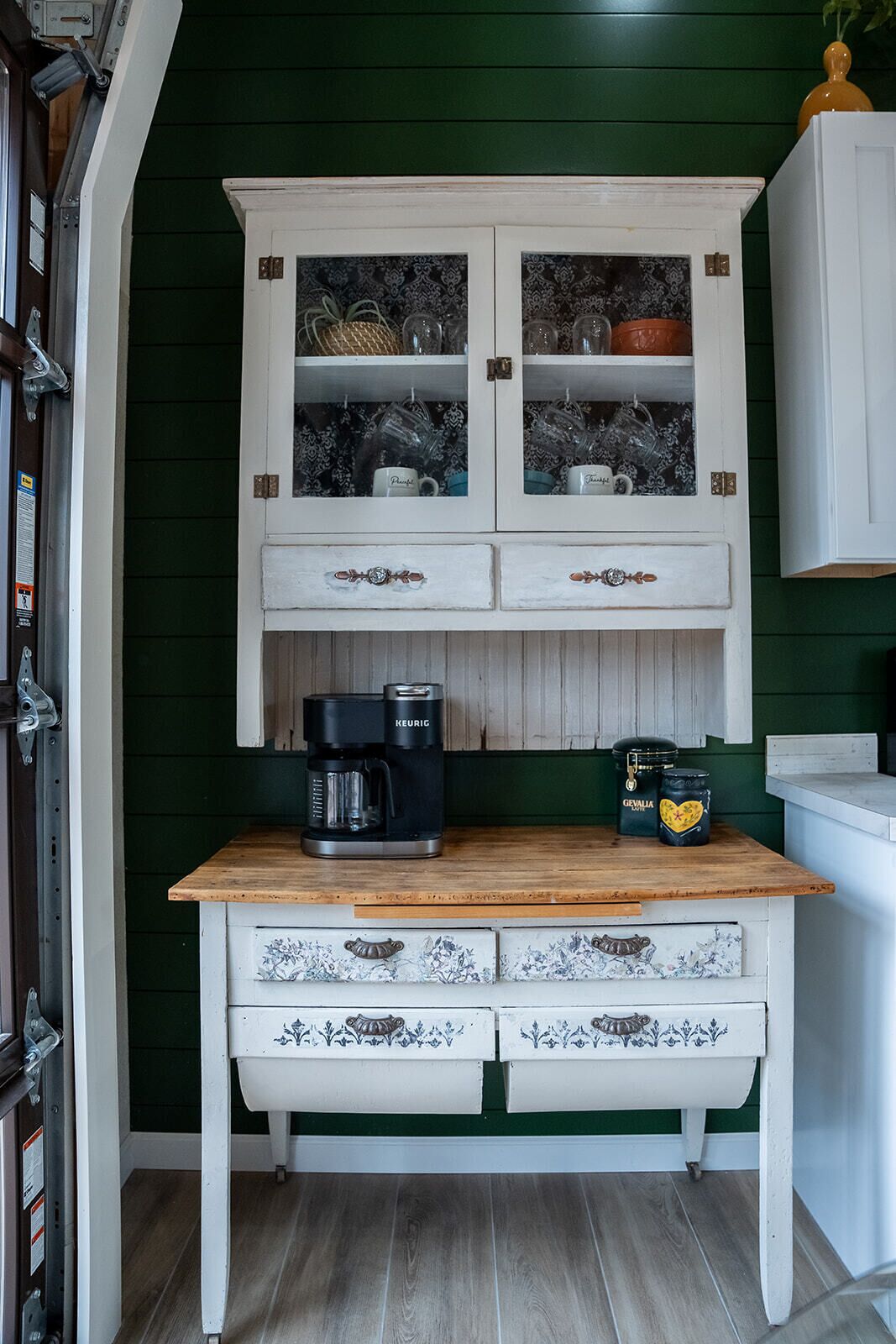 A kitchen with a wooden countertop, a coffee maker, a kettle, and a cabinet with glass doors.
