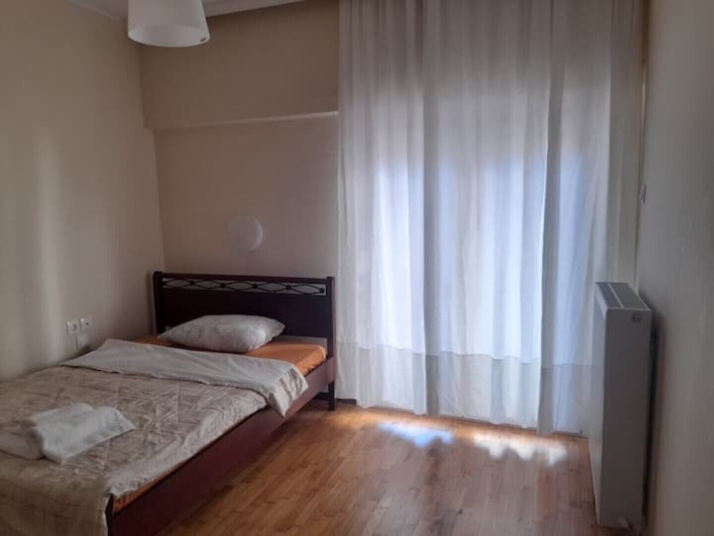 Ein Schlafzimmer mit Holzboden, einem Bett mit Kopfteil, einem Nachttisch, einer Lampe und einem Fenster mit Vorhängen.