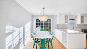 A modern kitchen with white cabinetry, a central island, and a dining area with a table and chairs.