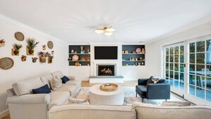 A spacious living room with a fireplace, a sofa set, a coffee table, and a large window offering a view of the outdoors.