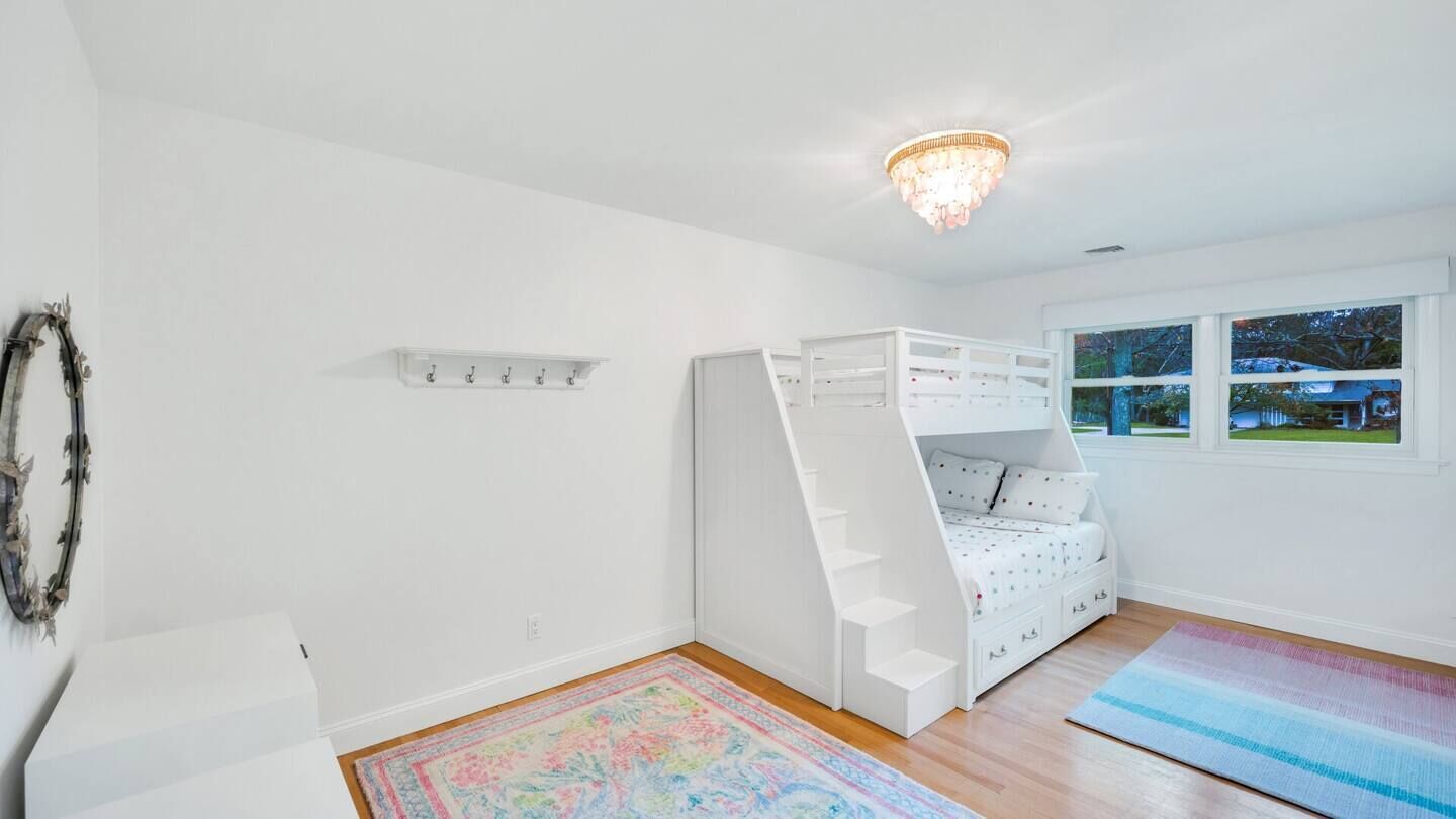 A child’s bedroom with a bunk bed, a chandelier, a window with a view, and a colorful rug.