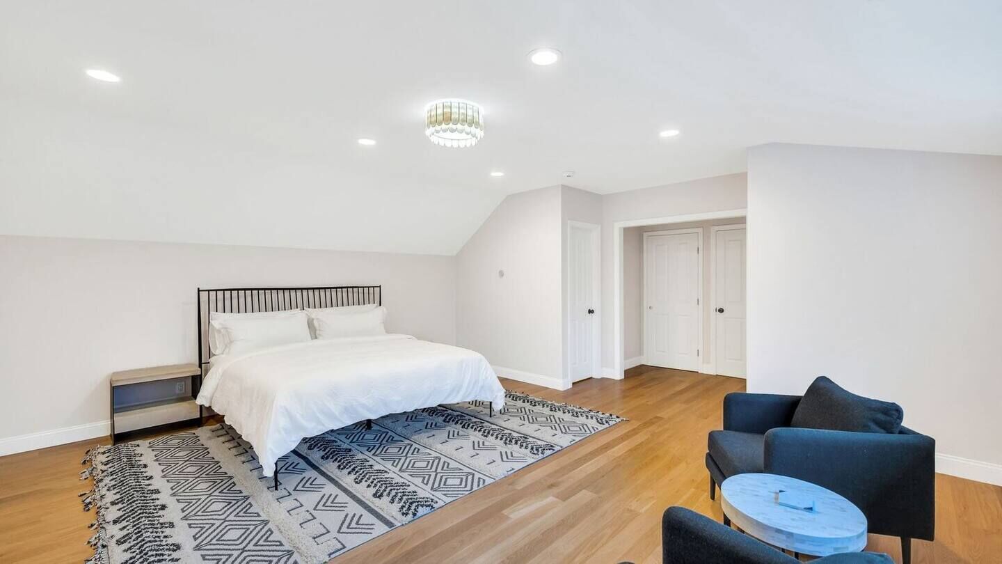 A bedroom with a bed, a nightstand, a chair, a small table, and a patterned rug.