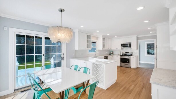 A modern kitchen with white cabinetry, a central island, and a dining area with teal chairs.