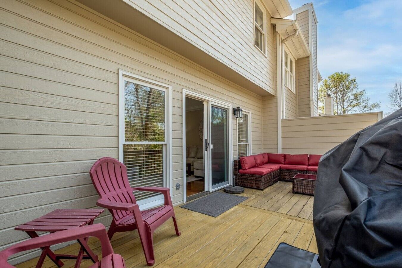 Eine überdachte Terrasse mit einem roten Adirondack-Sessel, einer roten Couch und einem Grill.