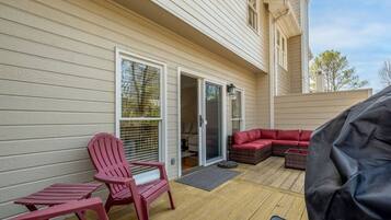 Eine überdachte Terrasse mit einem roten Adirondack-Sessel, einer roten Couch und einem Grill.