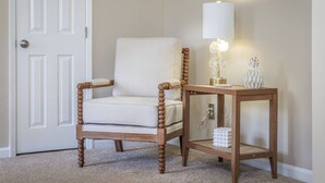 Une chaise en bois dotée d’un siège et d’un dossier rembourrés, placée à côté d’une petite table en bois sur laquelle se trouvent une lampe et des objets décoratifs.