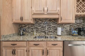 A kitchen with wooden cabinets, a granite countertop, a stainless steel sink, and a mosaic backsplash.
