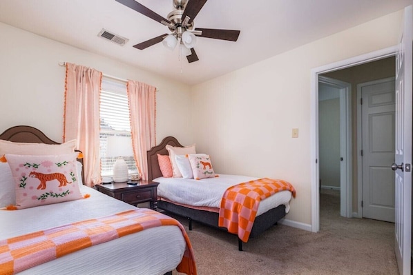 A bedroom with two beds, a ceiling fan, a window with curtains, and a door.