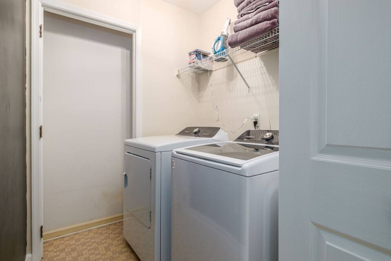 Une buanderie équipée de deux machines à laver, d’un étendoir à linge avec des serviettes et d’une porte.