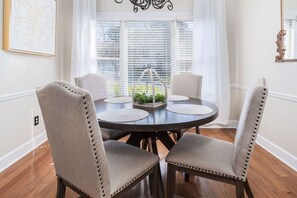 Een eetkamer met een ronde tafel, vier stoelen, een decoratief middelpunt en een raam met jaloezieën.