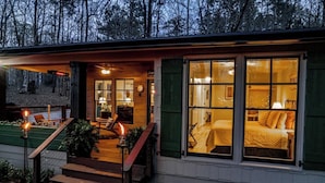 Ein gemütliches Blockhaus mit Veranda, ein Bett, das durch das Fenster sichtbar ist, und eine Treppe, die zum Eingang führt.