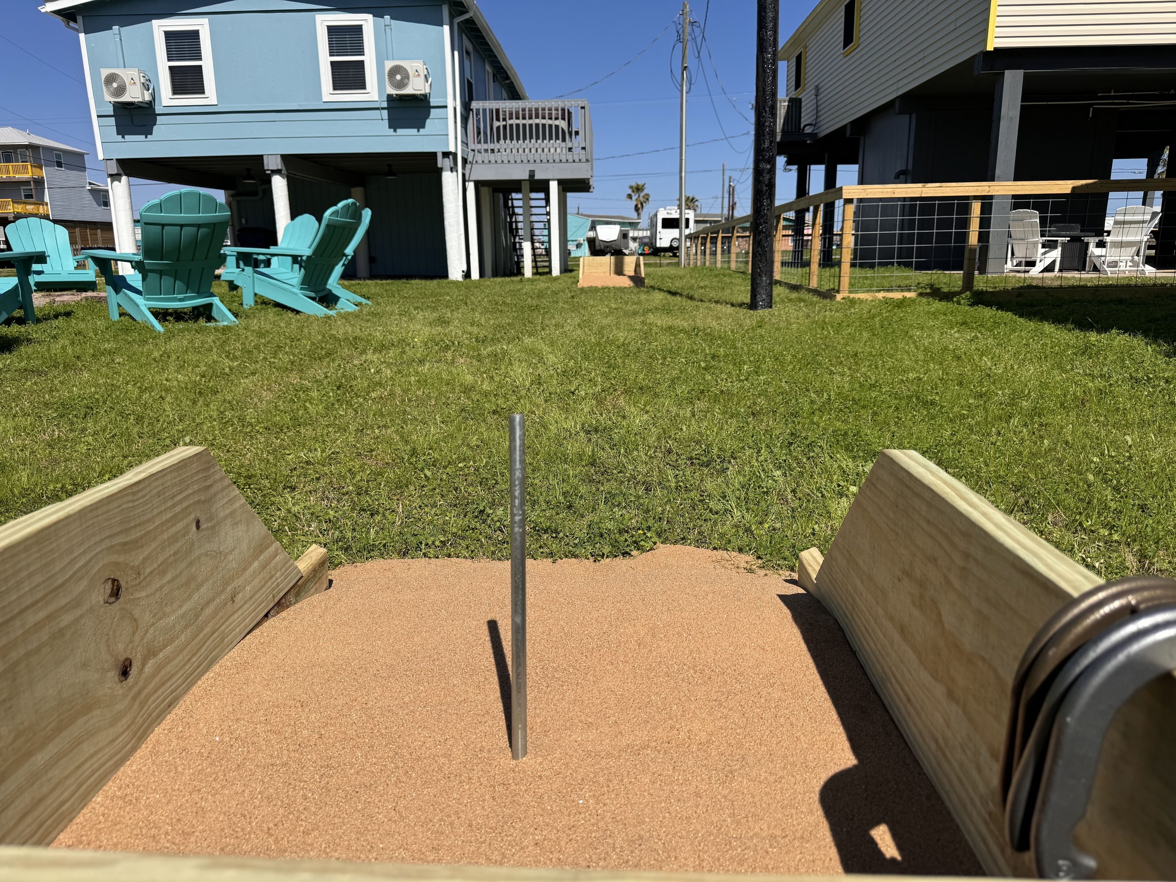 A backyard with a sandbox, wooden play area, and a blue house with air conditioning units.