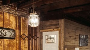 A rustic wooden interior with a dining table and chairs, a hanging light fixture, and a door with a window.